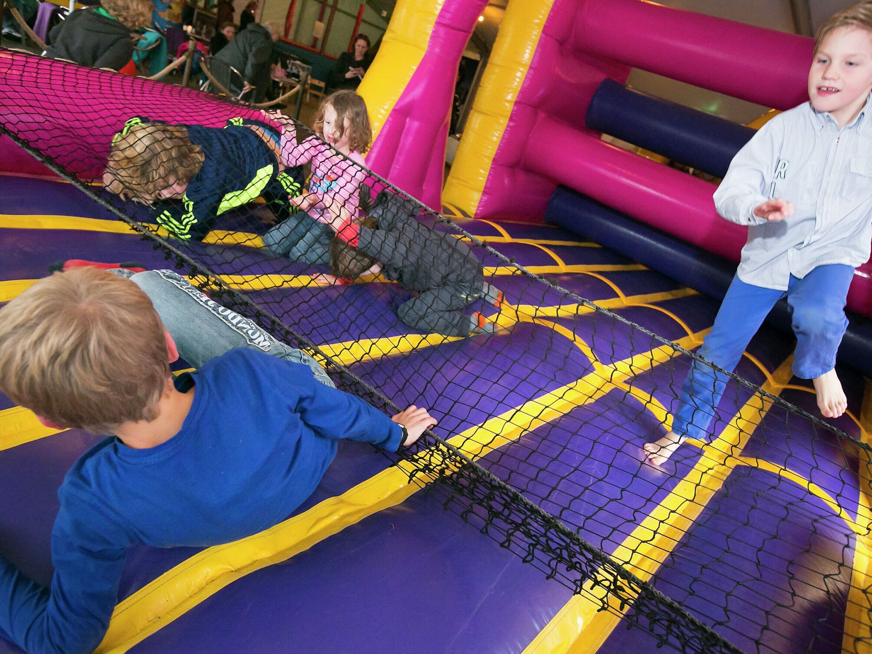Children playing on a colorful indoor play area with netted sections and inflatable structures.