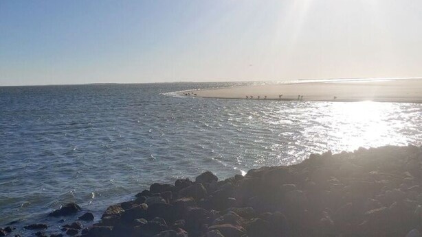 A beach with a rocky shoreline and calm sea. - Holiday Apartment Kapteins Kamers (Borkum)