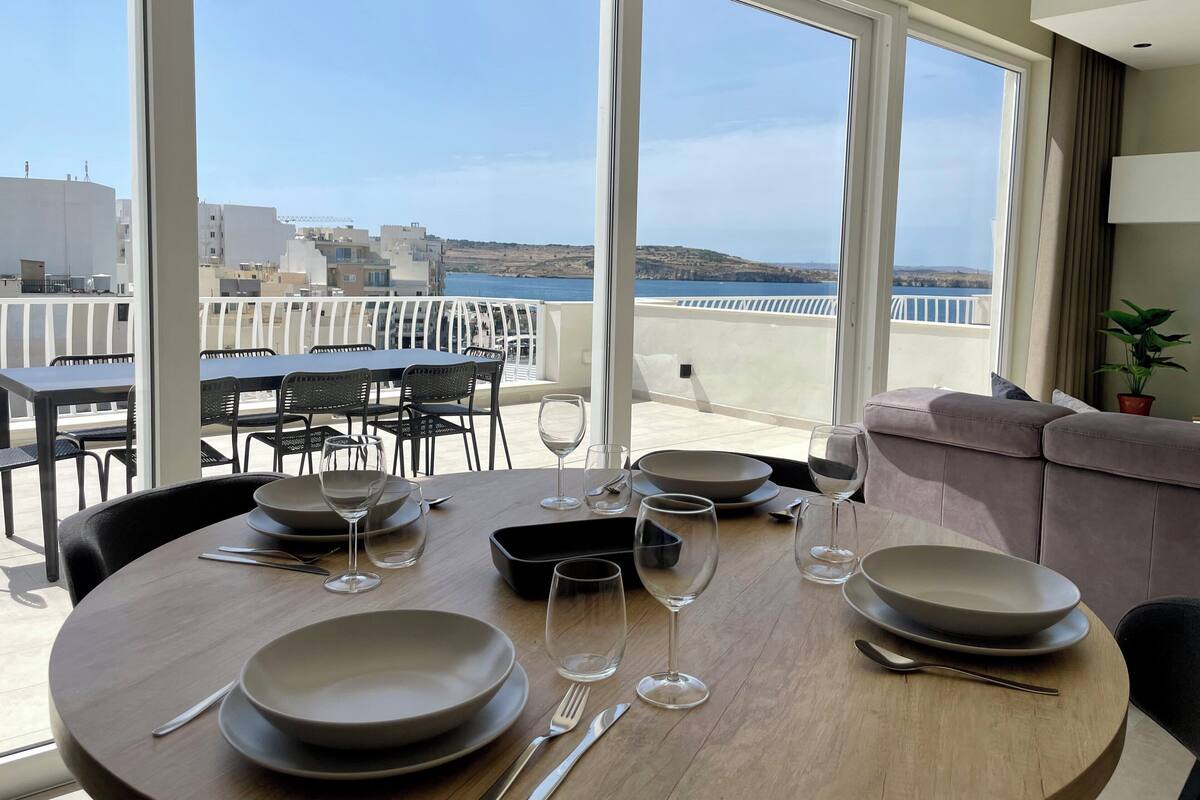 A dining area with a view of the sea, a balcony with outdoor seating, and a potted plant.