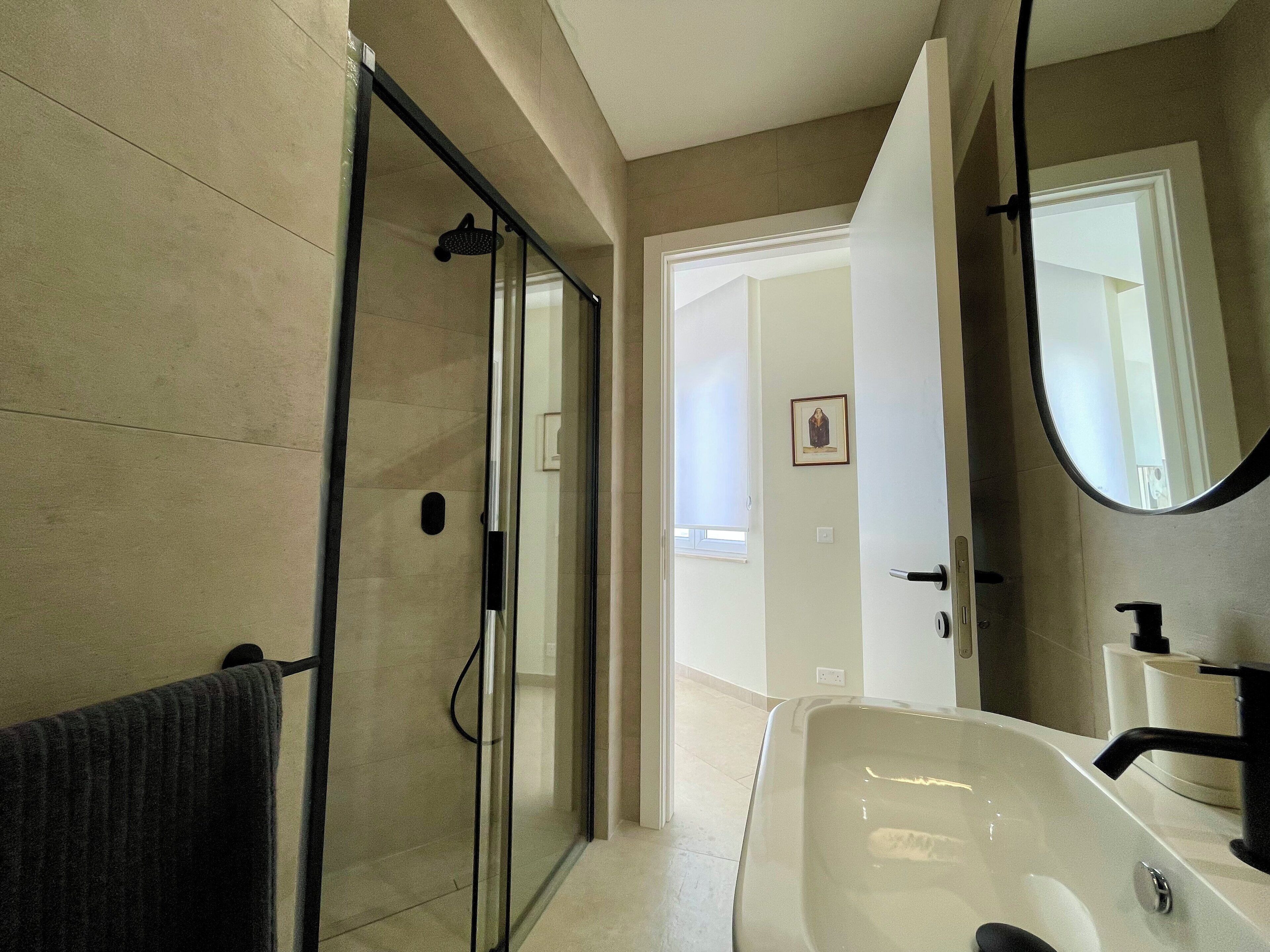 A modern bathroom with a glass shower enclosure, a large sink, and a mirror.