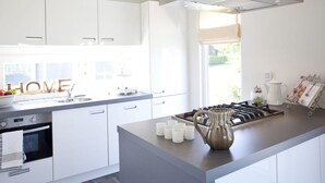 Eine moderne Küche mit weißen Schränken, einem eingebauten Backofen, einem Gasherd und einem großen Fenster, das für natürliches Licht sorgt.