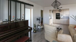 A modern living room with a piano, a beige sofa, and a kitchen in the background. - Nice apartment with balcony in Pré-Saint-Gervais (Le Pré-Saint-Gervais)