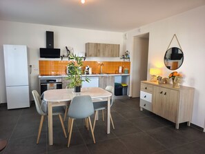 A modern kitchen with a dining table, chairs, a refrigerator, an oven, and a sink. - T2 apartment with terrace (Ajaccio)