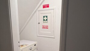 Ein Waschraum mit Waschmaschine, kleinen Stauraumschrank und einem Notausgangsschild.