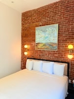 A bedroom with a brick wall, a painting, and two wall-mounted lamps.