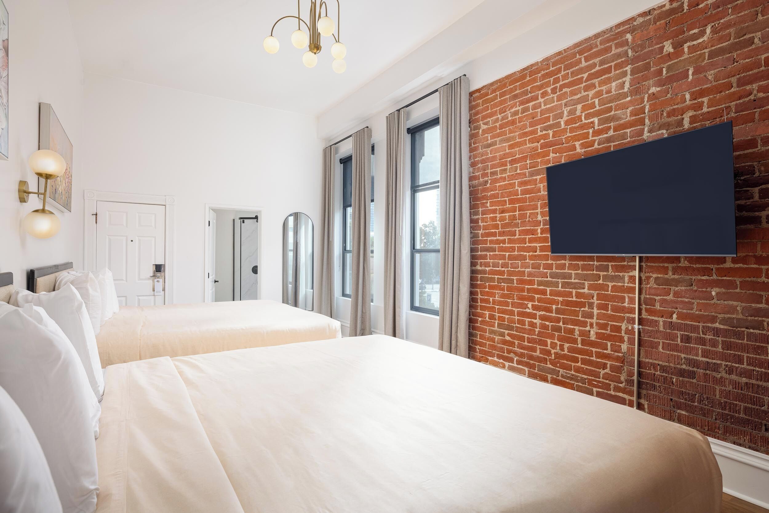 Habitación de hotel con dos camas, una pared de ladrillo, un televisor de pantalla plana y un candelabro.