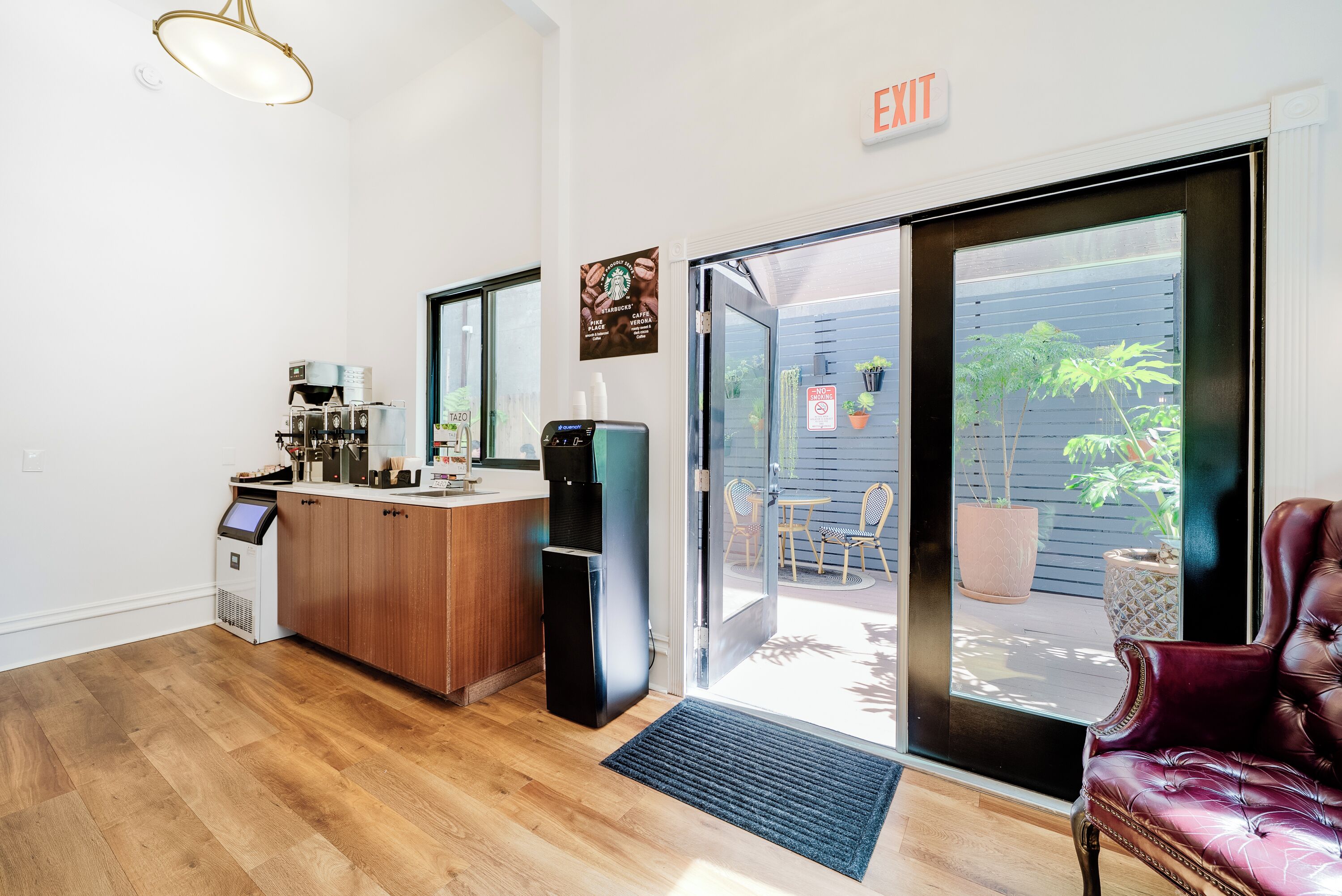 Un intérieur moderne avec un plancher en bois, un coin bar équipé d’une machine à café, d’un réfrigérateur et d’un fauteuil rouge moelleux.