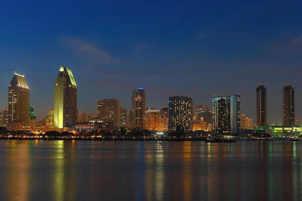A nighttime city skyline with illuminated buildings reflecting on the water. - The Beau Hotel Gaslamp Quarter San Diego (San Diego)