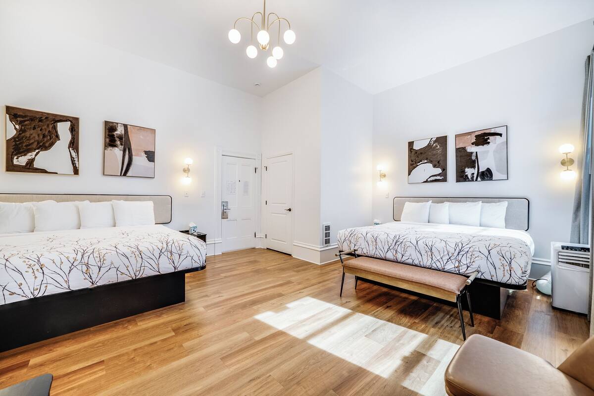 Une chambre d’hôtel avec deux lits, un banc, un bureau et un radiateur.
