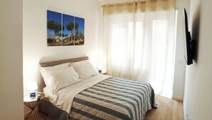 Een slaapkamer met een bed, nachtkastje, lamp, televisie aan de muur en een raam met gordijnen.