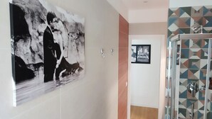 Een moderne badkamer met een groot abstract schilderij, een douche met geometrische tegels en een klein, ingelijst fotootje aan de muur.