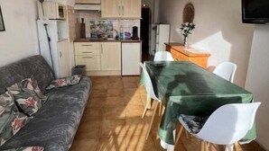 Un espacio habitable compacto con kitchenette, un comedor con mesa y sillas, y un sofá.