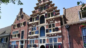 Un bâtiment historique à la façade symétrique, doté de nombreuses fenêtres avec volets et d’une entrée centrale en arc de cercle.