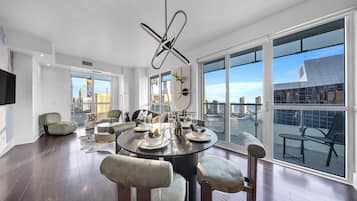 A modern dining area with a round table, chairs, and a city view through large windows.
