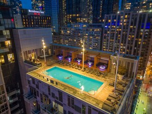 Una piscina en la azotea con tumbonas y zona de bar, rodeada de edificios altos.