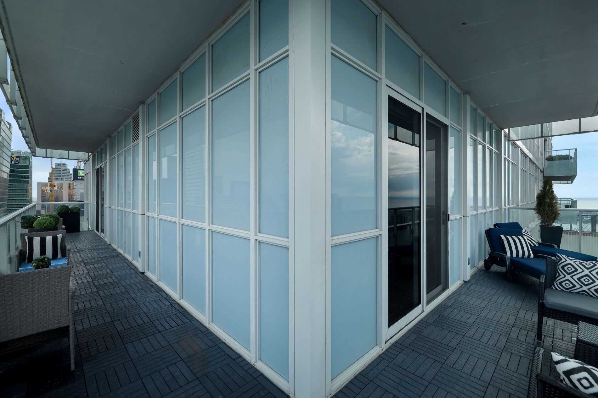 Un balcón moderno con pared de vidrio, una zona de estar con mesa y sillas, y vista a la ciudad.
