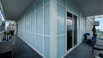 Un balcón moderno con pared de vidrio, una zona de estar con mesa y sillas, y vista a la ciudad.