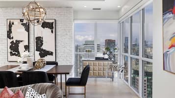 A modern living space with a dining area, a sofa, and a view of the cityscape through large windows.