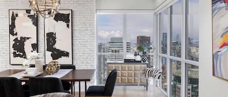 A modern living space with a dining area, a sofa, and a view of the cityscape through large windows.