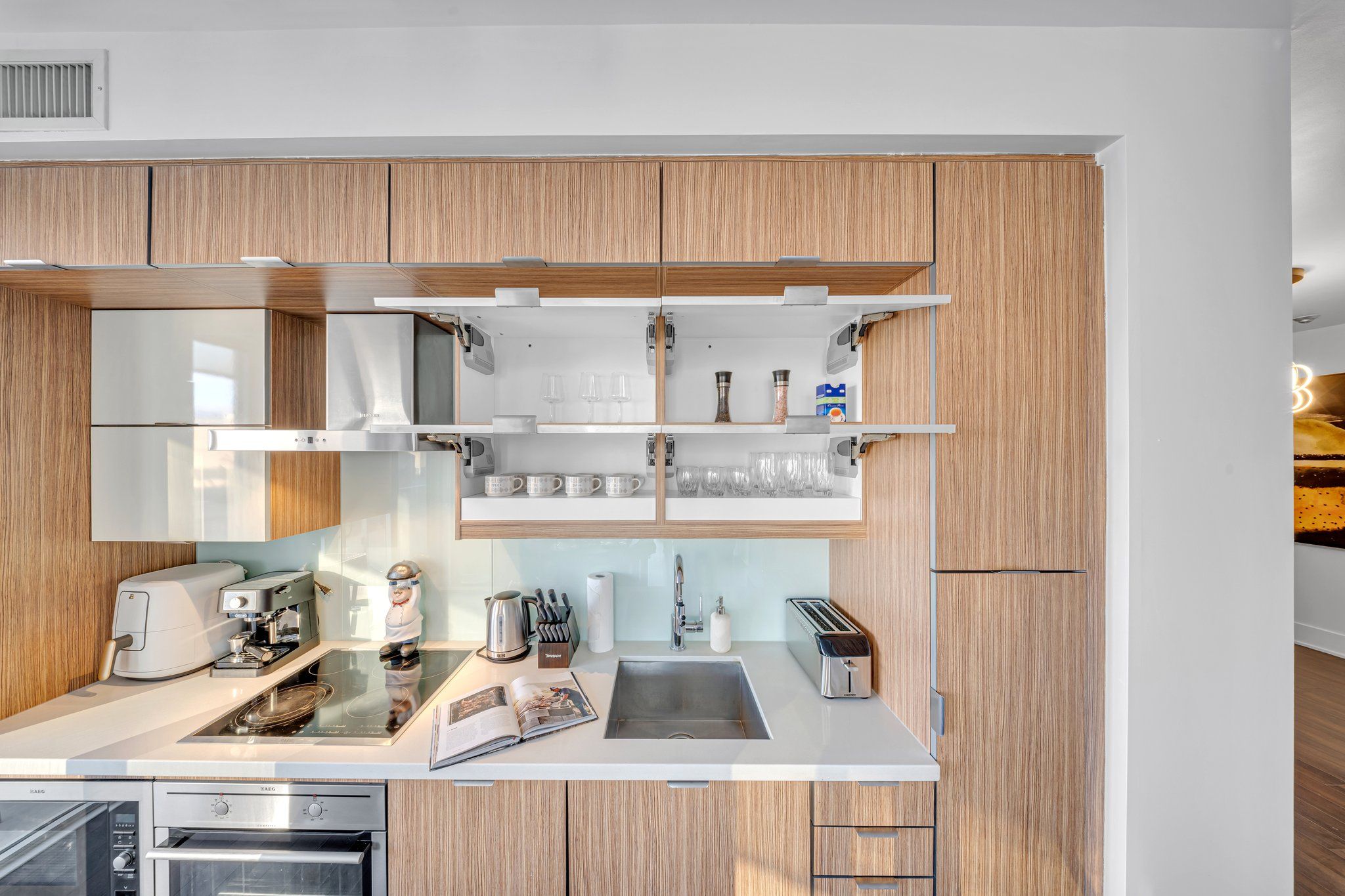 A modern kitchen with wooden cabinets, a built-in oven, a coffee machine, and a toaster.