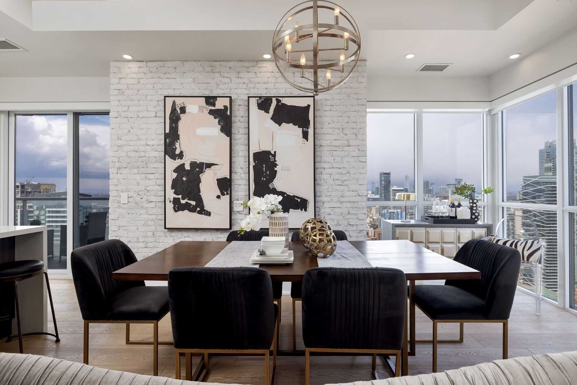 Un comedor moderno con pared de ladrillo, arte abstracto, una araña y vistas a la ciudad.