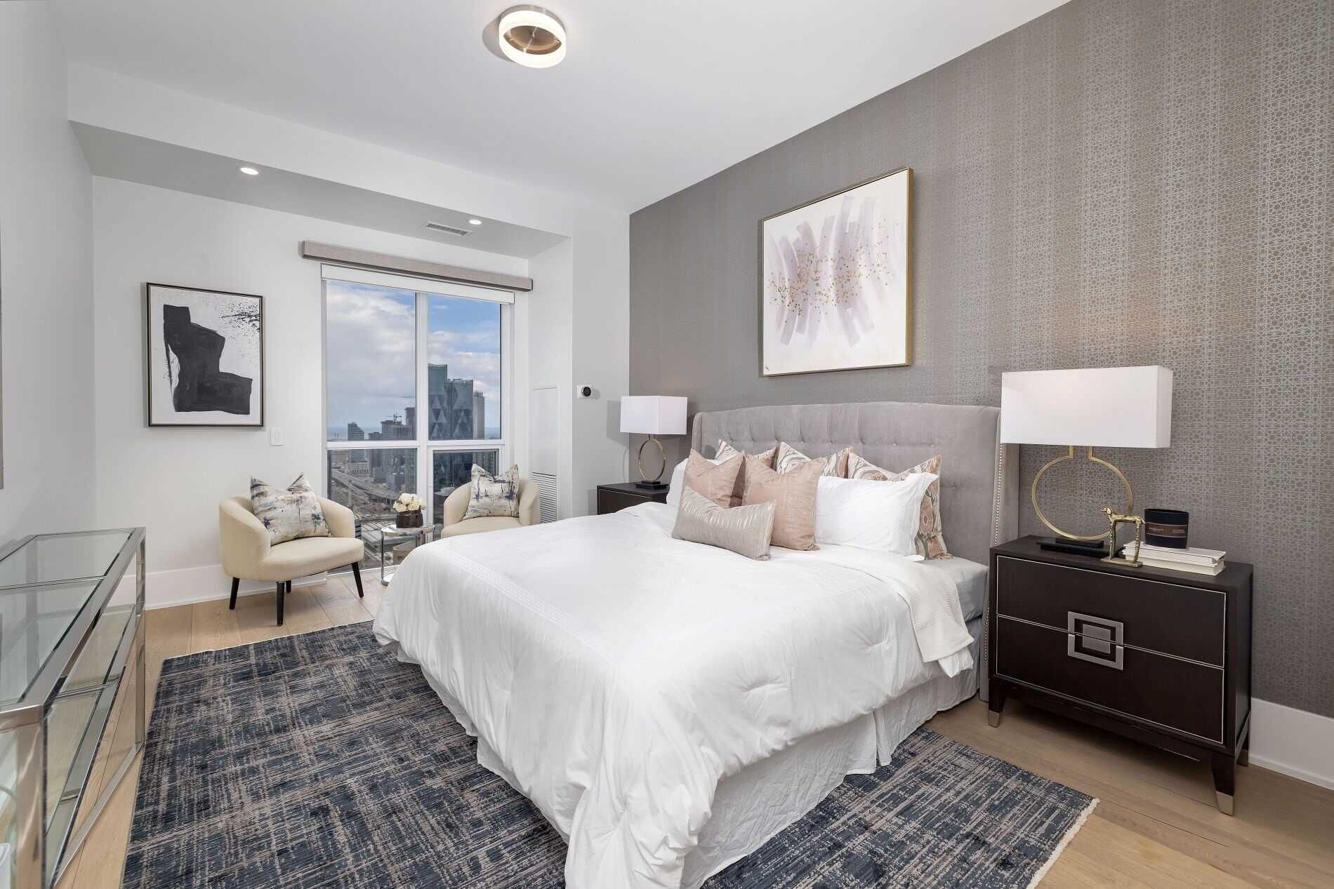 A modern bedroom with a large bed, two bedside tables, a glass coffee table, and a city view.