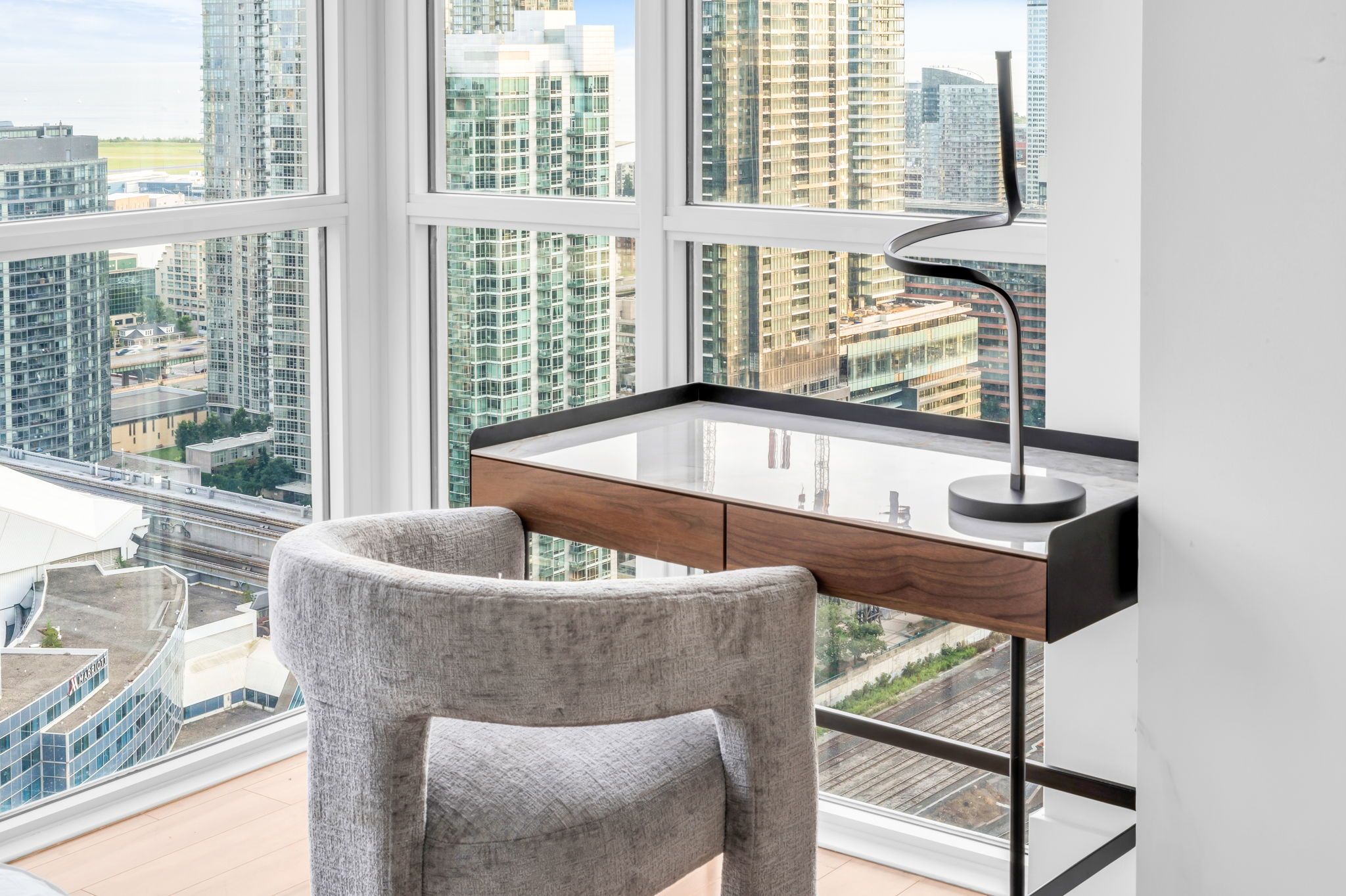 Un espacio de oficina moderno con escritorio, silla y grandes ventanales con vistas a un paisaje urbano.