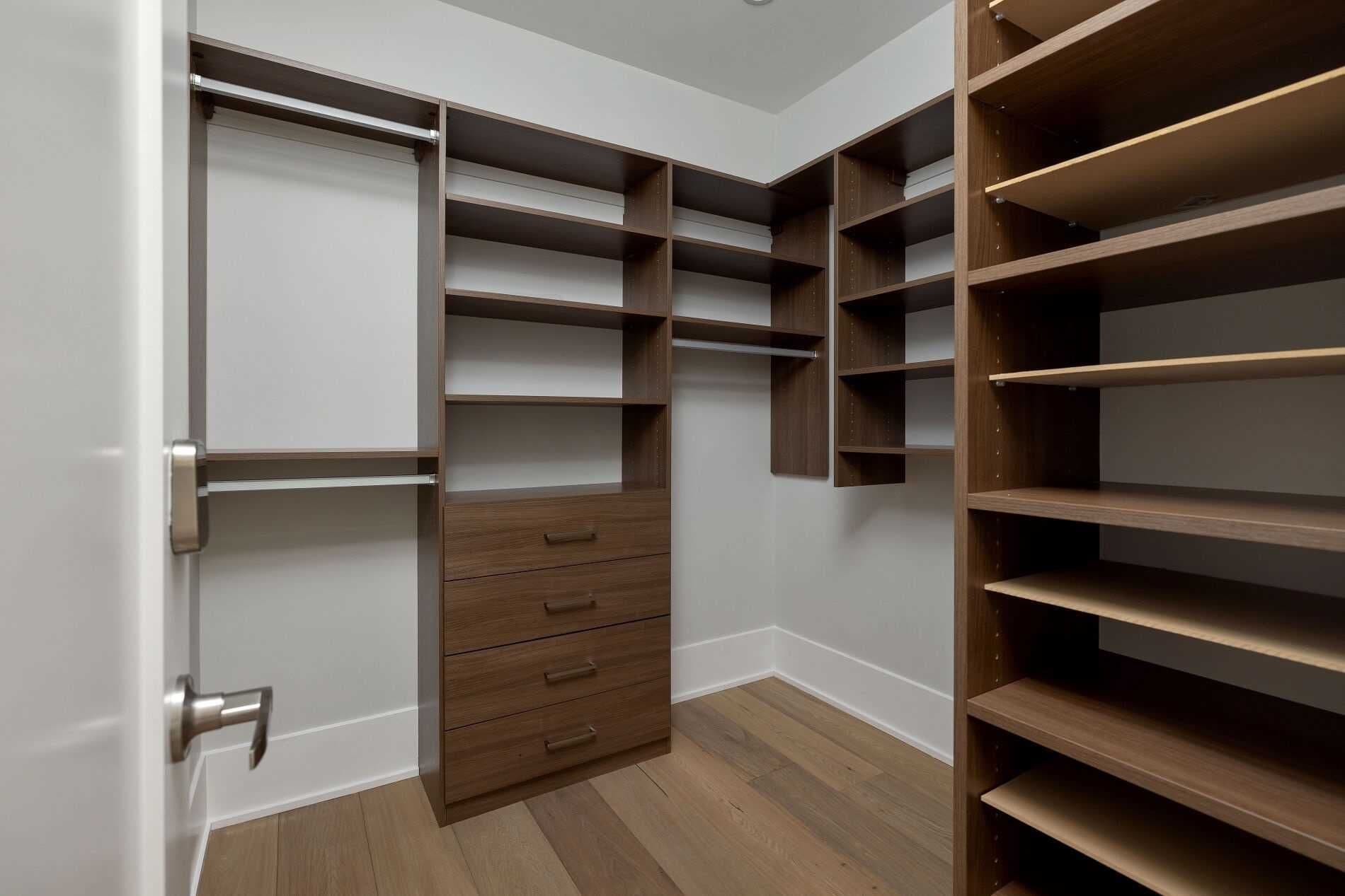 A walk-in closet with multiple shelves and drawers, a door with a silver handle, and wooden flooring.