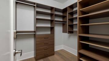 A walk-in closet with multiple shelves and drawers, a door with a silver handle, and wooden flooring.