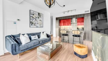 A modern living room with a sofa, coffee table, and ottoman. There is a kitchen area with red cabinets and a dining set.