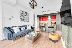 A modern living room with a sofa, coffee table, and ottoman. There is a kitchen area with red cabinets and a dining set.