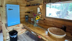 Eine kleine Küche mit einem blauen Kühlschrank, Holzschränken, einer Holz Arbeitsplatte, einem Spülbecken und einem Fenster mit Blick auf Bäume.