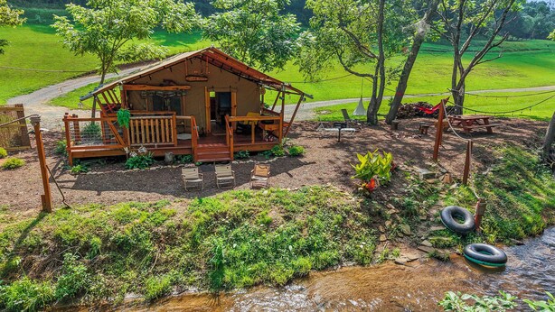 Eine Holzhütte mit Veranda, umgeben von viel Grün und einem kleinen Bach.