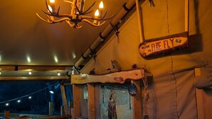 Ein rustikales Blockhäuschen im Inneren, mit Holzbalkendecke, einem Kronleuchter, einem Willkommen-Schild, einem Traumfänger und einem Tisch mit Stühlen.