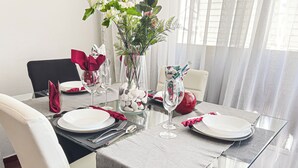 Mesa de comedor dispuesta para seis personas, con platos blancos, servilletas rojas y copas de cristal.