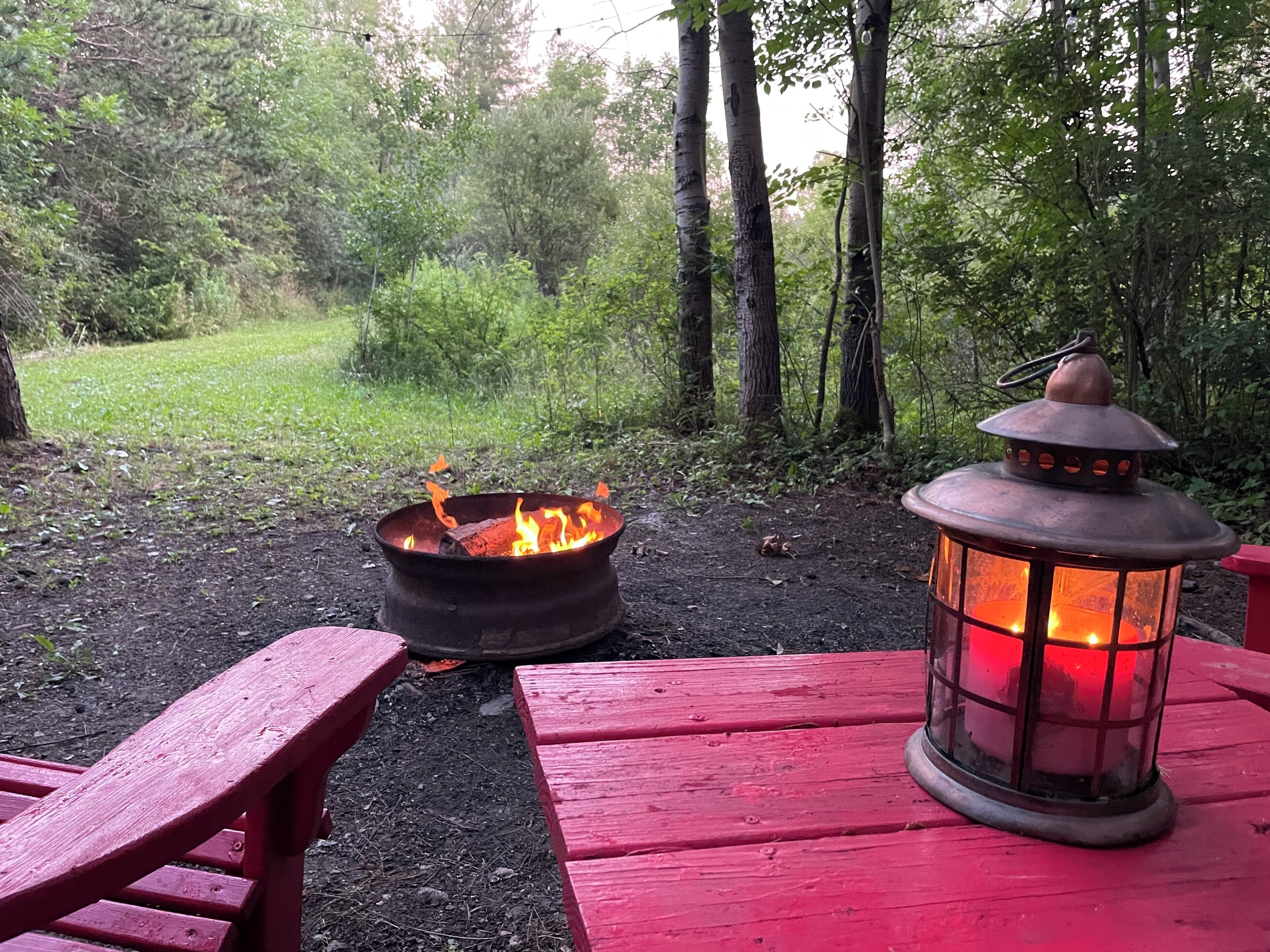 A campfire with a lantern on a wooden table in a forested area.