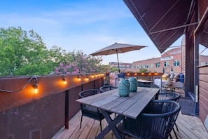 An outdoor patio with a wooden table and chairs, string lights, and a large umbrella. - 2BR Designer Condo East Downtown Austin (Austin)