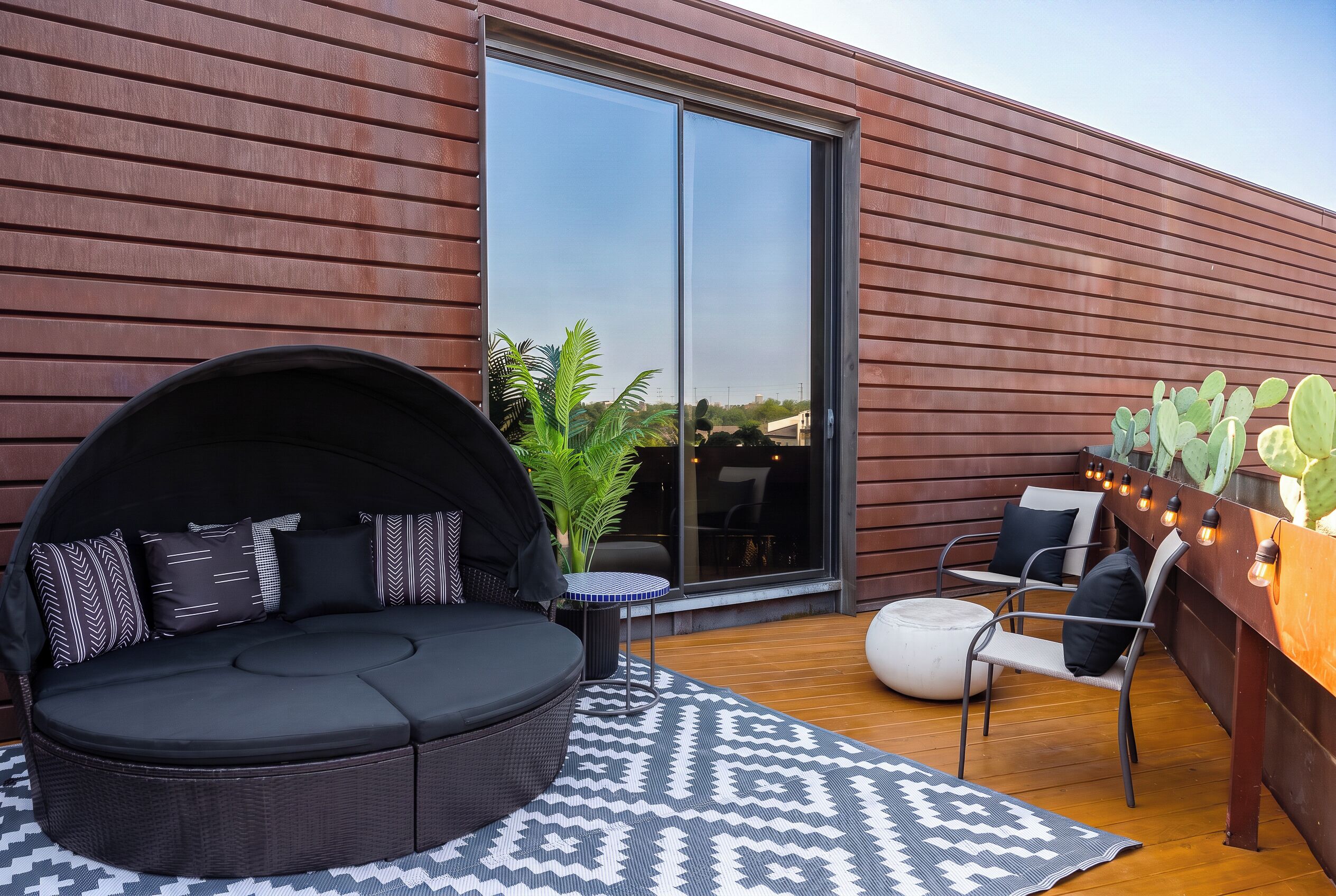 A modern outdoor seating area with a round black sofa, patterned cushions, a small round table, and a patterned rug.