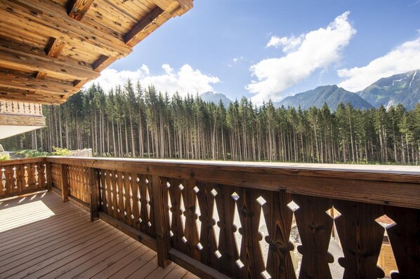 A wooden deck with a railing overlooking a forest and mountains. - Chalet in Neukirchen Near Anfangerpiste (Neukirchen am Grossvenediger)