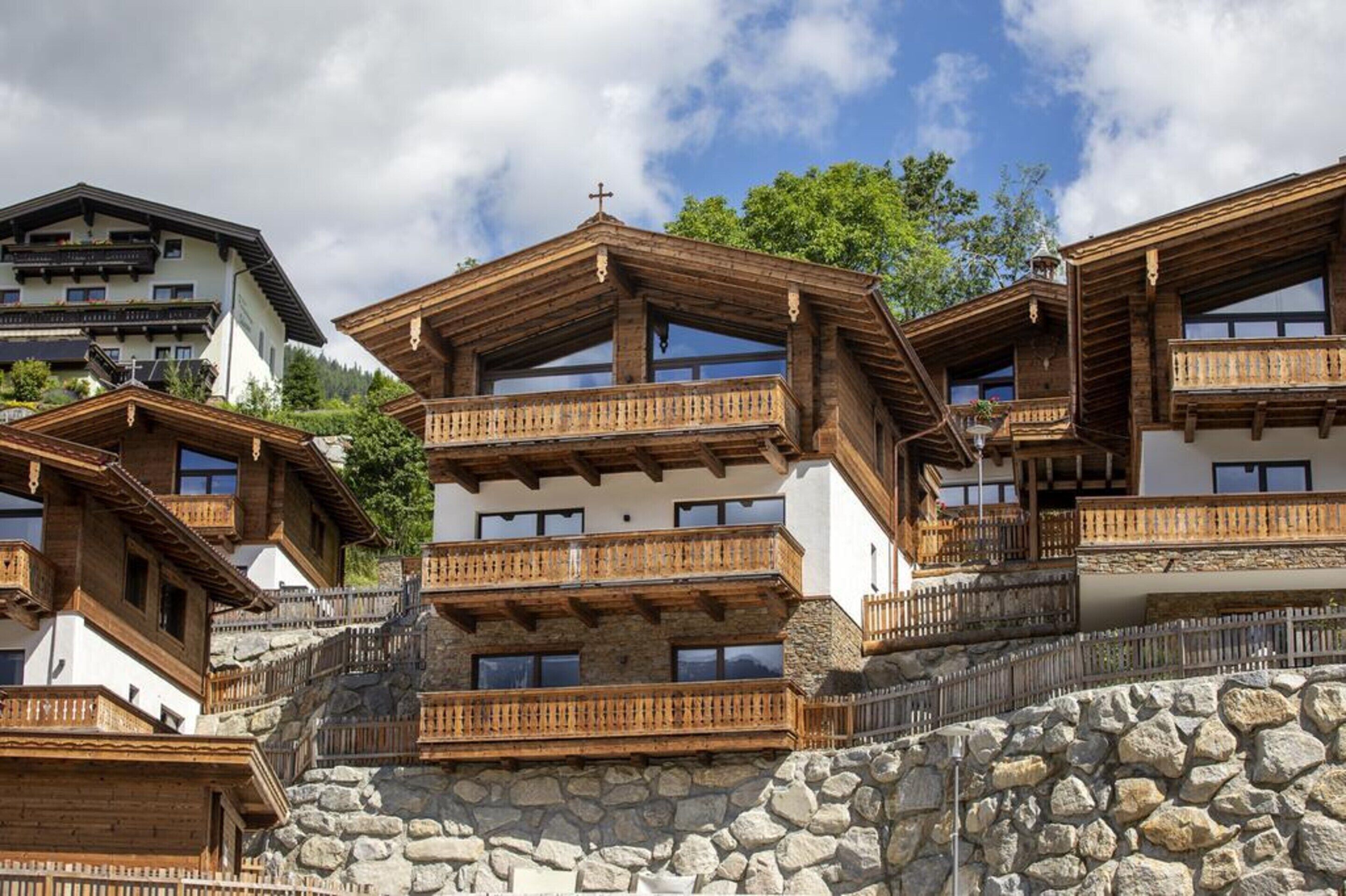 Un ensemble de chalets de montagne en bois, dotés de balcons, de murs en pierre et d’une croix sur le toit.