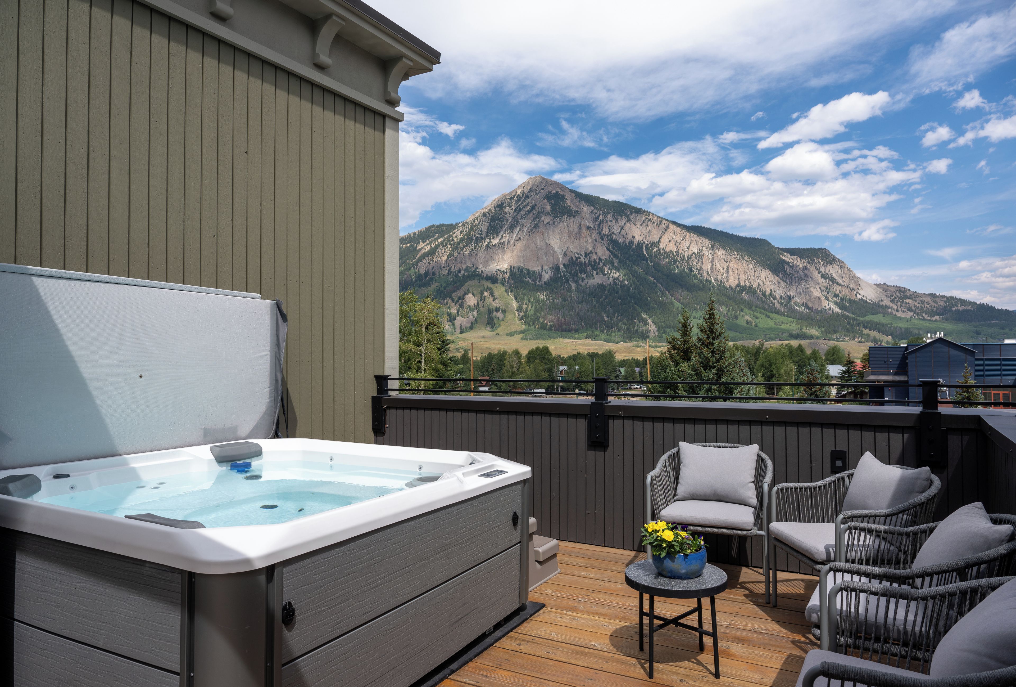 A hot tub on a deck with wicker chairs and a mountain view.