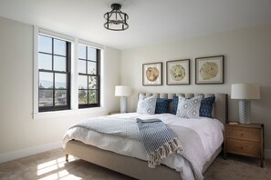 A bedroom with a large bed, two bedside lamps, a nightstand, and three framed artworks on the wall.