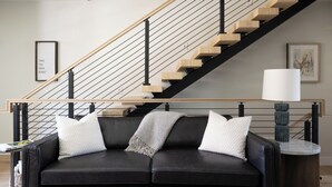 Ein modernes Wohnzimmer mit einem schwarzen Ledersofa, einer Holztreppe und einem gerahmten Bild an der Wand.