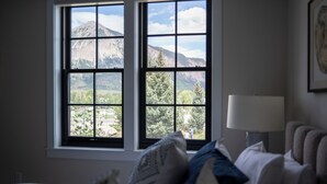 Ein Schlafzimmer mit großem Fenster, einem Bett, einem Nachttisch und einer Lampe.