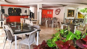 A restaurant with multiple dining tables and chairs, a bar area, and a variety of plants in the foreground. - Classic Doble (Santander)