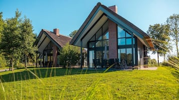 Una casa moderna con un amplio frente de vidrio, techo inclinado y césped cuidado.