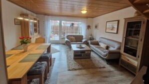 A spacious living room with a wooden dining table, two sofas, and a coffee table. - Holiday Home Rubin Comfortable Vacation Home (Norden)