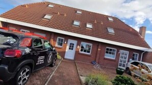 A two-story house with a red-tiled roof, a brick driveway, and a small garden area with rocks and shrubs. - Holiday Home Rubin Comfortable Vacation Home (Norden)