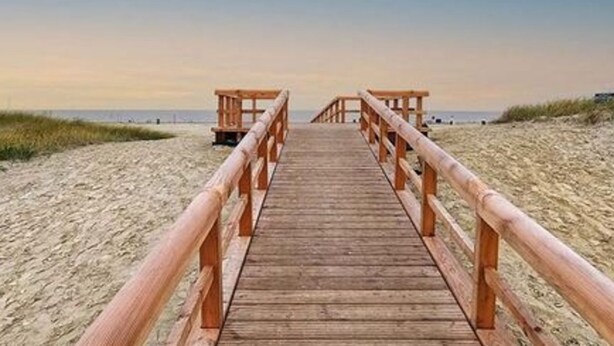 A wooden boardwalk leading to beach huts, surrounded by sand dunes. - Holiday Home Rubin Comfortable Vacation Home (Norden)