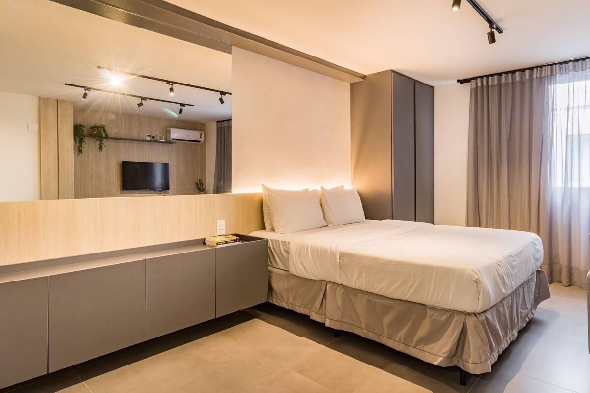Quarto moderno com uma cama grande, televisão integrada e mesa de cabeceira.